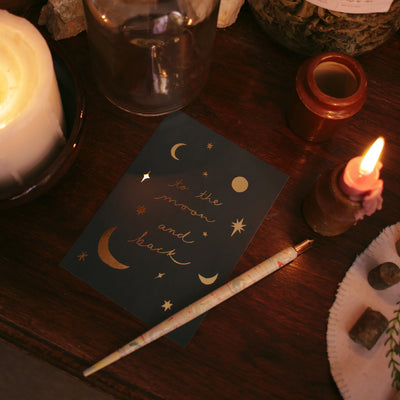 gold foil moon and back postcard on a candlelit table