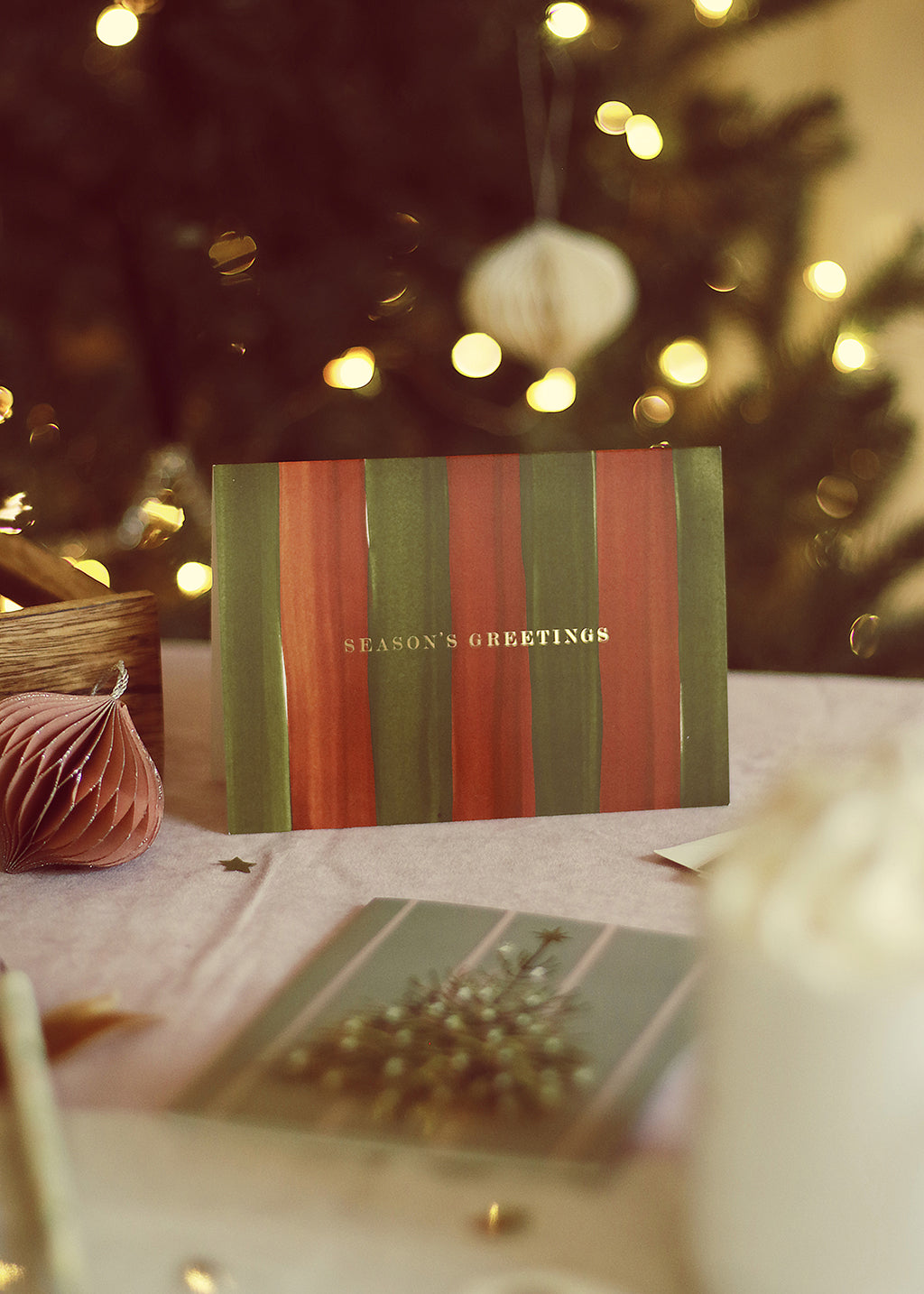 a red and green christmas card with handpainted stripes. Reads "seasons greetings" in gold foil