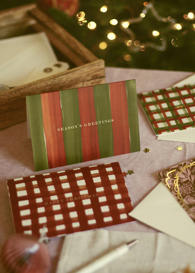 a red and green striped christmas card walongside other festive greetings on a pink tableclotth